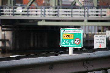 distance sign in green in hectometers on road N207 at 24,4. Sign is placed by provence Zuid Holland and show also speed limit of 50