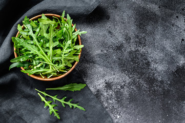 Fresh arugula in a wooden bowl. Black background. Top view. Copy space