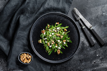 Healthy salad with arugula, goat cheese, nuts and vinaigrette sauce. Black background. Top view