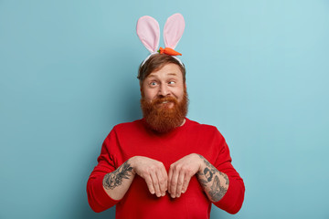 Funny ginger man pretends being Easter bunny, goes crazy, crosses eyes, keeps palms like rabbit,...