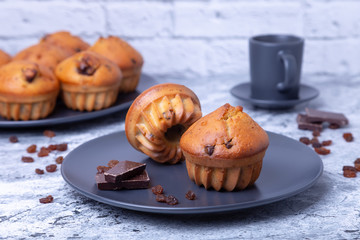 Muffins with chocolate and raisins. Homemade baking. In the background is a plate with muffins and a cup of coffee. Close-up.