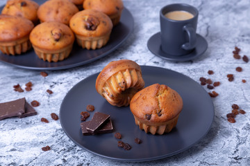 Muffins with chocolate and raisins. Homemade baking. In the background is a plate with muffins and a cup of coffee. Close-up.