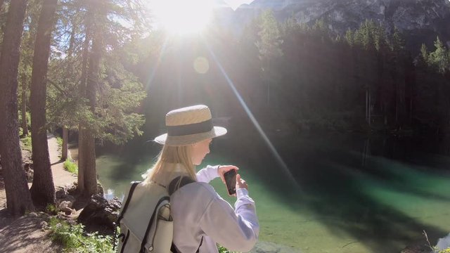 Young caucasian woman tourist making picture on modern mobile phone camera exploring scenic landscape of Apls, breathtaking nature of forest and lake in mountains, female blogger photographing