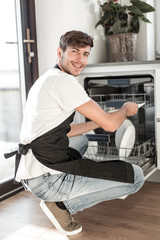 handsome young man sitting near an open dishwasher