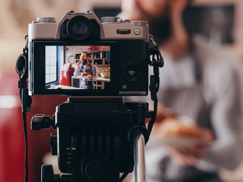 Culinary vlog. Home cooking. Bakery food. Camera on tripod recording male chef eating fresh croissant.
