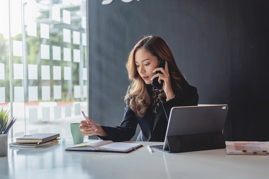 Attractive Young Asian Woman Talking On The Mobile Phone And Standing At Her Working Place In Office.