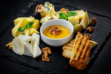 Cheese plate with cheeses Dorblu, Parmesan, Brie, Camembert and Roquefort in serving on the black textured background