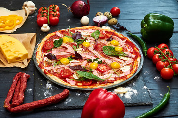 Raw pizza with mozzarella cheese, meat, tomatoes, mushrooms, peppers, herbs on a dark wooden...