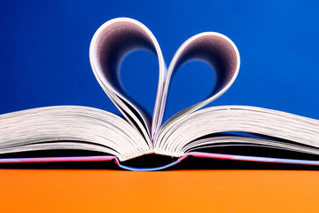 An open book with a folded heart of pages on a blue and yellow background.