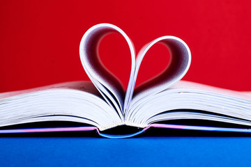 An open book with a folded heart of pages on a red and blue background.