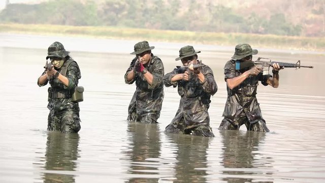 A group of military in war paint black and green face mark wearing green army uniform hiding soak in water their hands holding weapons aiming left and right 