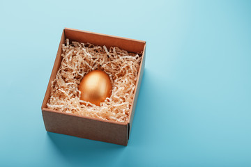 Egg made of gold in a wooden box on a blue background. The concept of exclusivity and superprize. Minimalistic composition.