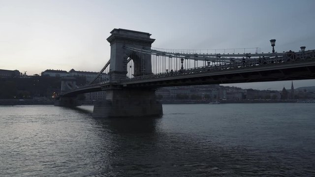 Handheld middle shot of Chain Bridge during sunset, orange grey sky in Budapest. Handheld shot of Chain Bridge on background of Fisherman's Bastion in winter