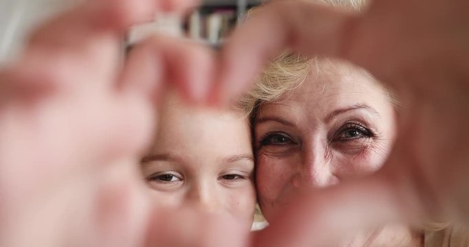 Affectionate grandmother and granddaughter making heart gesture looking at camera