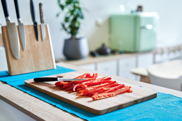 Strips of red pepper cut on a wooden board in a modern house. Shallow depth of field
