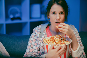 Portrait shot of the woman with popcorn sitting on the sofa watching something scary while eating...
