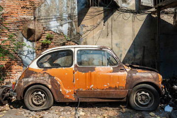 The old orange Fiat cars are old and decaying. They are parked beside the old buildings in the Talad Noi community.