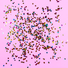 Gold colorful confetti on pink background. Festive backdrop of sparkles for birthday, carnival