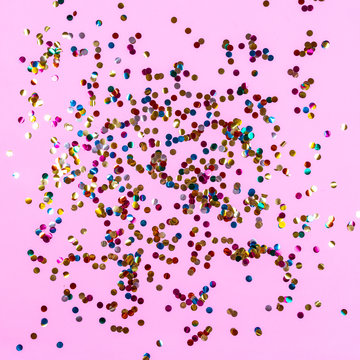 Gold colorful confetti on pink background. Festive backdrop of sparkles for birthday, carnival