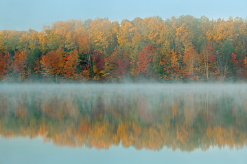 Autumn landscape at dawn of Moccasin Lake in fog with mirrored reflections in calm water, Hiawatha National Forest, Michigan's Upper Peninsula, USA