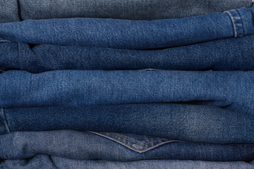Pile of denim blue jeans texture in the classic indigo style in different tints. Close up shot,...