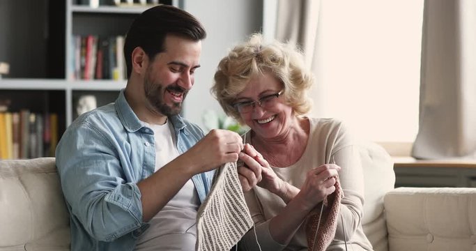 Funny happy adult son helping senior mother knitting laughing together