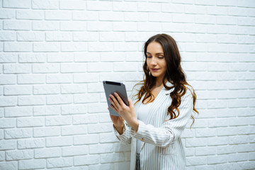 serious young business woman with dark long hair in white clothes holds a tablet in her hands running and slides near a white wall © ostap_davydiak