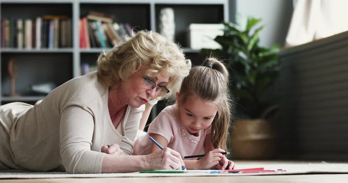 Older grandmother teaching preschool granddaughter drawing pencils together