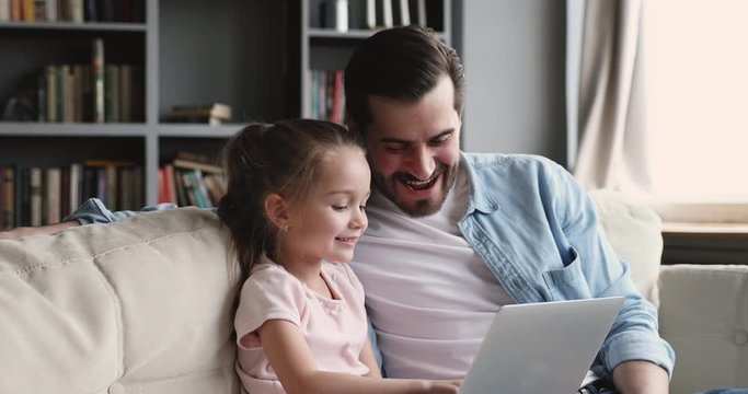 Smiling adult dad teaching kid daughter using laptop at home
