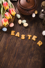 Happy Easter background, Lettering from cookies, tulips and colorful quail eggs in metal basket on wooden background.