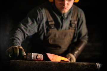 A man in protecting headphones working with hot metal knife blank