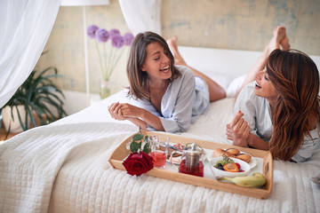 lesbians smiling surprised by breakfast in bed in casual sleepwear. morning, fresh, fun, lesbian concept