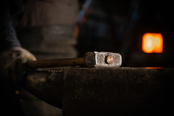 A hammer on the anvil in workshop - a man worker standing on the background