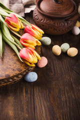 Happy Easter background with tulips and colorful quail eggs in metal basket on wooden background. Copy space.