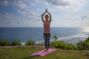 Yoga pose. Woman practicing yoga. Young woman raising arms with namaste mudra. Outdoor yoga on the...