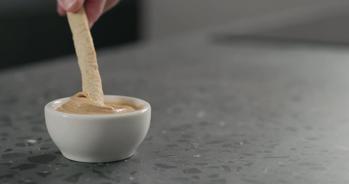 Slow motion man hand dip grissini in cashew paste in white bowl on terrazzo countertop