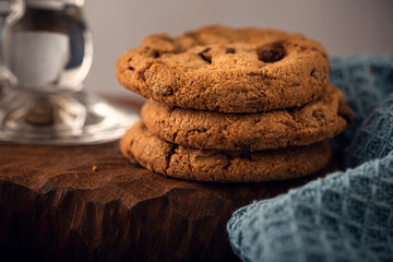Chocolate chip cookies on green plate with glass of coffee on old wooden table. Selective focus.