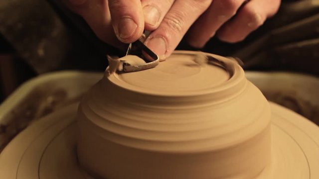Ceramic art. Creative hobby. Male hands carving clay bowl bottom on spinning wheel.