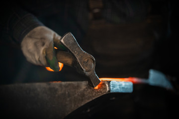 Blacksmith forging a knife out of the hot metal using a hammer - holding the knife in forceps