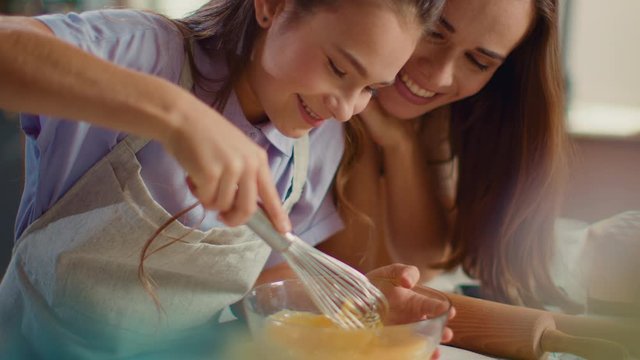Woman and girl whisking eggs on kitchen. Daughter and mother cooking together