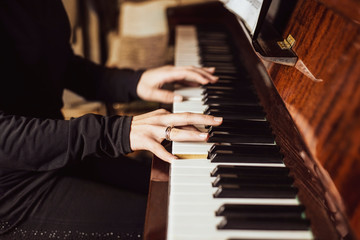 The young girl is resting at home and playing on the piano with pleasure. Her fingers play a familiar melody smoothly and rhythmically
