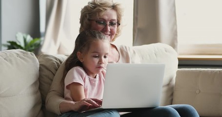 Smiling older grandmother and granddaughter using laptop together on sofa - Powered by Adobe