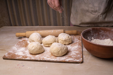 A woman kneads the dough. Plywood cutting board, wooden flour sieve and wooden rolling pin - tools for making dough.