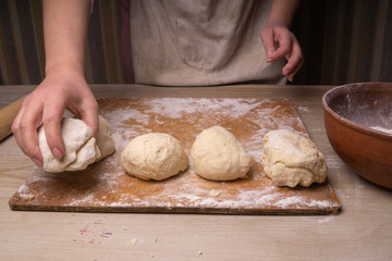 A woman kneads the dough. Plywood cutting board, wooden flour sieve and wooden rolling pin - tools for making dough.