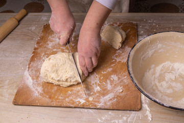 A woman kneads the dough. Plywood cutting board, wooden flour sieve and wooden rolling pin - tools for making dough.