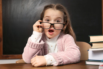 Cute little child wearing glasses at desk in classroom. First time at school