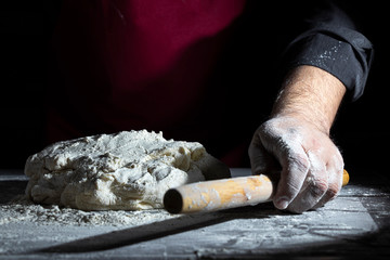 Male chef kneads dough on a wooden table. Dark background. Close-up.