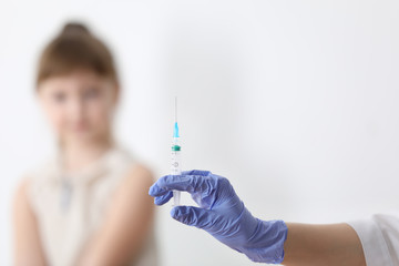 Doctor holding syringe with chickenpox vaccine and child on background, closeup. Varicella virus...