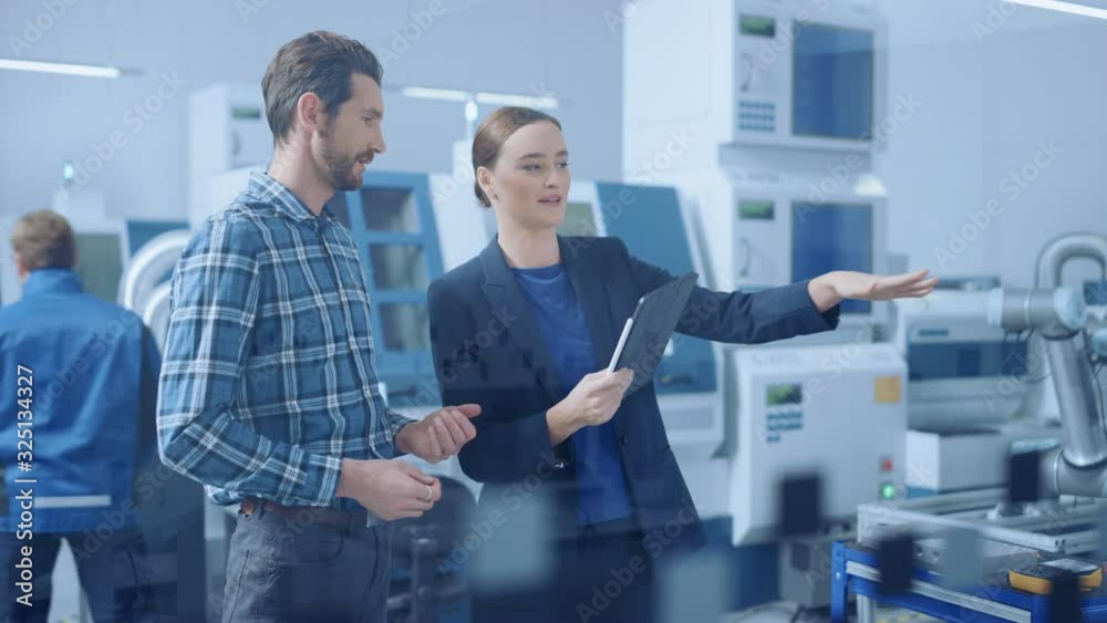 Poster Modern Factory: Female Project Manager and Male Engineer Standing, Talking, Using Digital Tablet for Programming and Monitoring Assembly Line. Industry 4.0 Facility with High-Tech CNC Machinery
