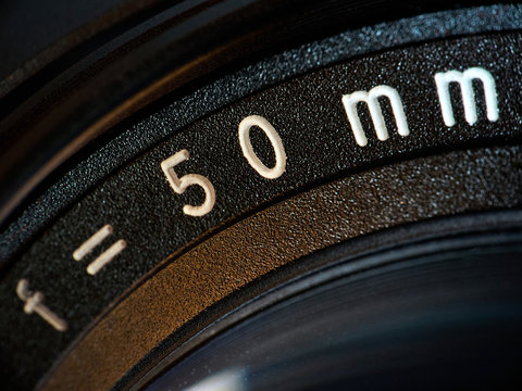 Extreme close up of 50mm inscription on old manual prime camera lens; vintage background and old technology; shallow depth of field; macro shot